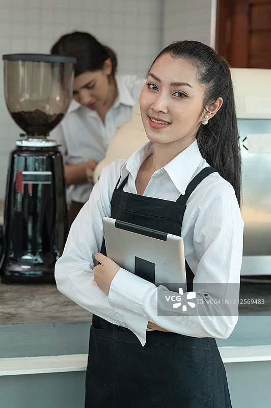 年轻的亚洲女咖啡师拿着平板电脑图片素材