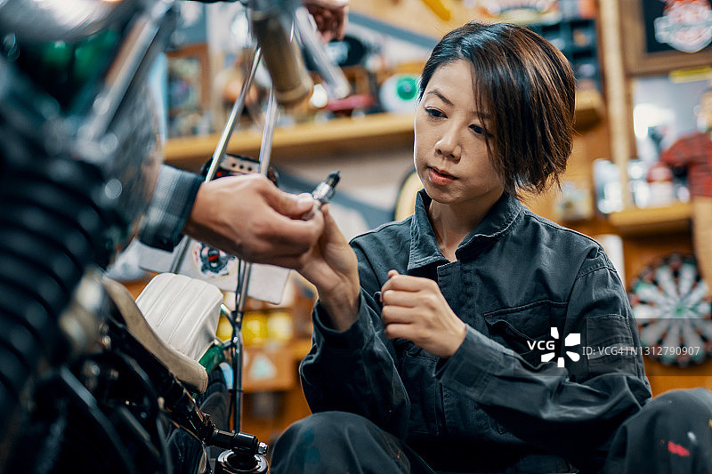 中年女性修车师在修车店学习摩托车修理图片素材