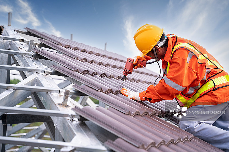 建筑工人在钢屋顶框架上安装新的瓦屋顶，屋顶工具，电钻用于新瓦屋顶，在建住宅图片素材