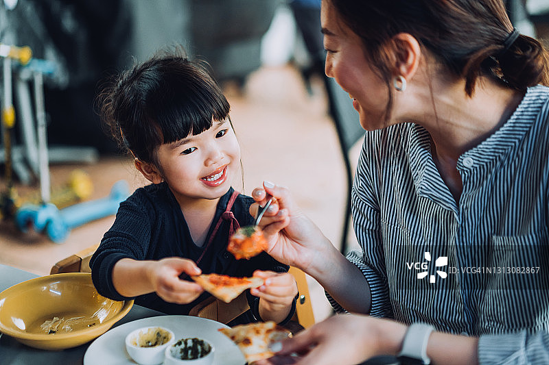 快乐的年轻亚洲母亲和可爱的小女儿在户外餐厅享受午餐，而母亲为女儿提供肉丸和肉酱面。家人享受亲密的时间和快乐的一餐在一起。家庭和外出就餐的生活方式图片素材