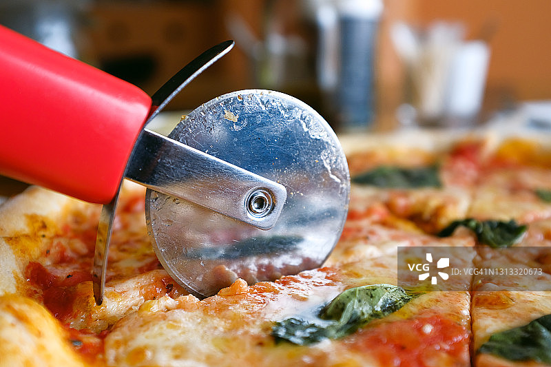 咖啡馆或快餐店里，一位女士用马苏里拉奶酪、番茄、罗勒切一块素食披萨。美味的意大利美食。切片玛格丽塔披萨在木板或支架上。美味不健康的午餐、小吃。图片素材