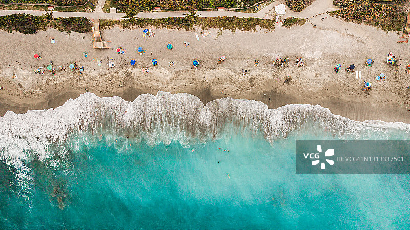 2021年4月2019冠状病毒病期间，佛罗里达州木星上充满活力的蓝绿色海洋海岸和彩色沙滩伞的直接空中俯瞰图片素材