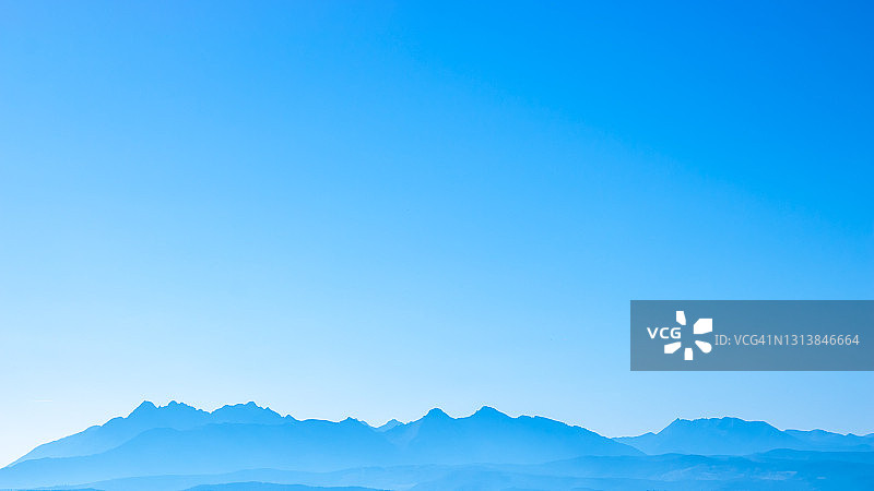 蓝色超现实的山脉映衬着青色的天空，梦幻般的童话般的山景图片素材