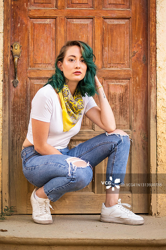 墨西哥城，一位绿色头发的年轻女子蹲在一扇木门前，看着镜头图片素材