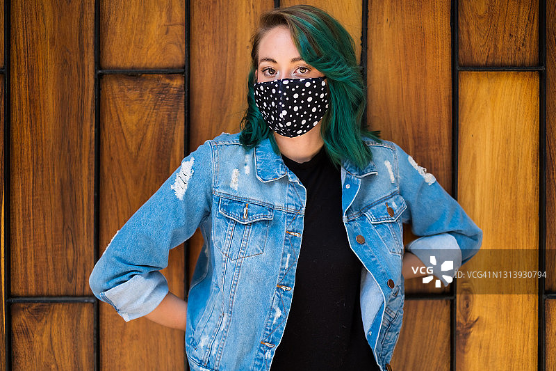 年轻女子绿色头发戴着面具，看着镜头在墨西哥城穿着牛仔夹克，木制背景图片素材