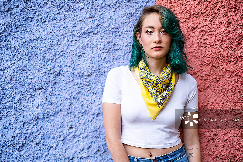 墨西哥城的一位年轻女子，在蓝色和红色背景的映衬下，一头绿色头发，正看着镜头图片素材