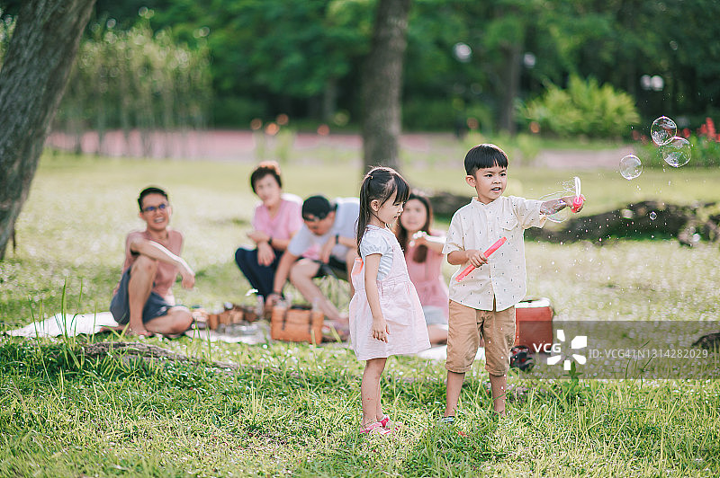 早上，在背光的阳光下，亚洲华人的孩子们拿着泡泡棒在公园里玩耍图片素材