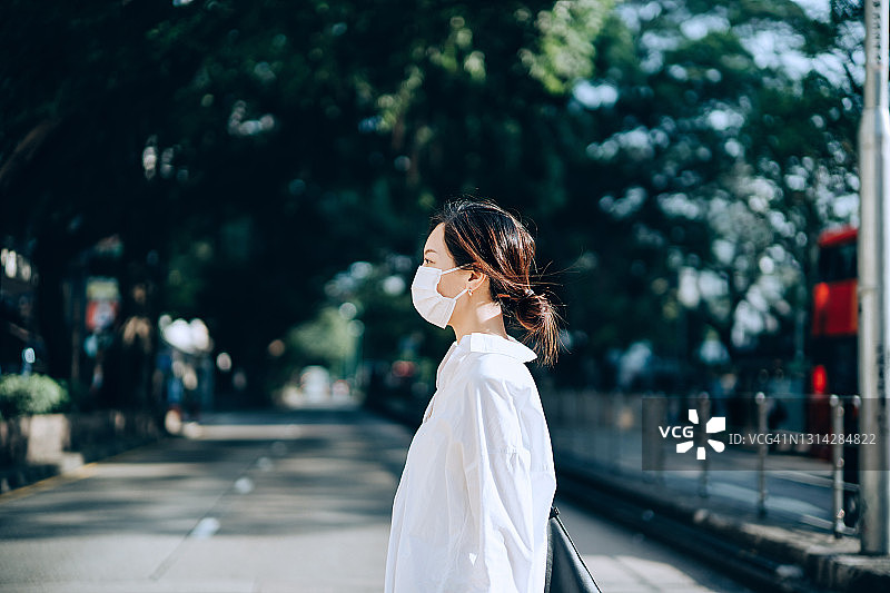 侧面的年轻亚洲妇女戴着保护面罩穿过街道，而在城市通勤。日常生活的新常态图片素材