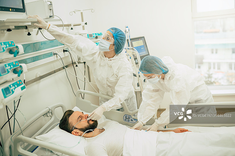 新冠肺炎患者在医院隔离病房，医生穿着防护服对其进行疾病治疗图片素材