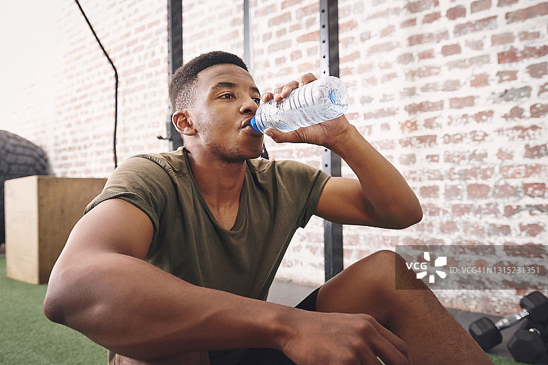 一个运动的年轻人在健身房喝一瓶水的照片图片素材