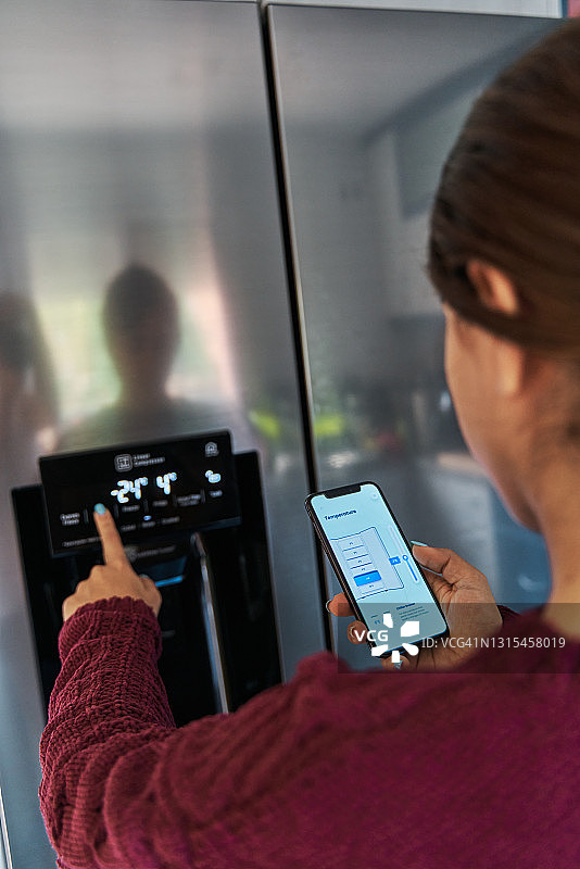 一名女性通过智能手机应用程序控制智能冰箱的温度图片素材