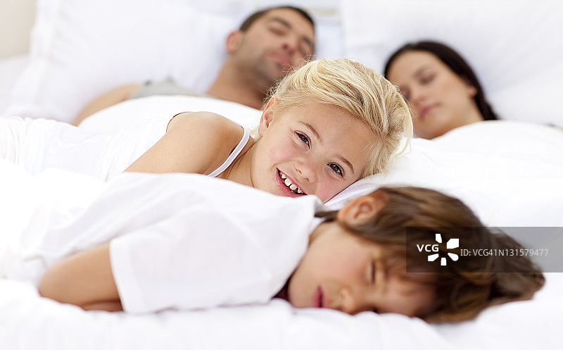 微笑的女儿放松她的哥哥和父母在床上图片素材