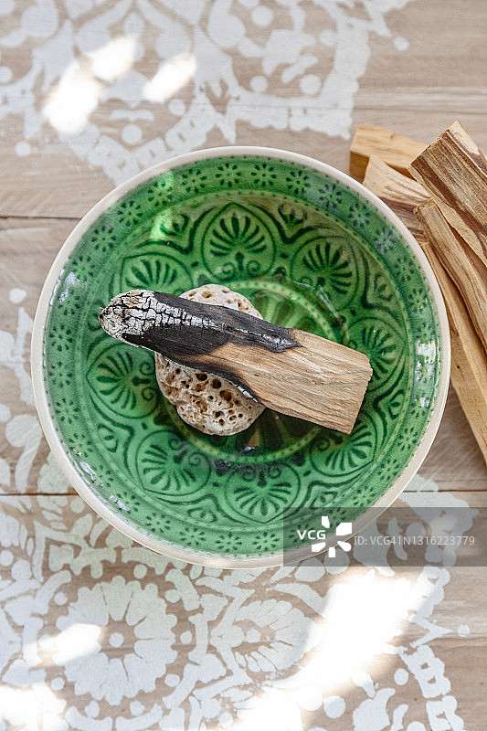 帕洛桑托的圣木(Bursera gravolens)放在一个绿色的陶瓷碗里，上面装饰着一个白色的曼荼罗。修行的概念。图片素材