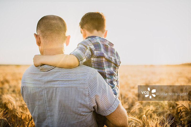 日落时分，父亲抱着儿子在田野上的背影图片素材