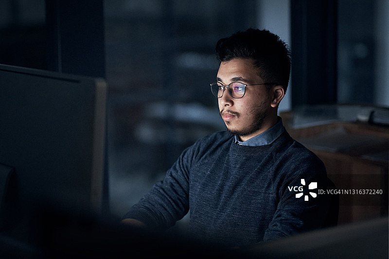 这是一个年轻商人深夜在现代办公室里使用电脑的照片图片素材