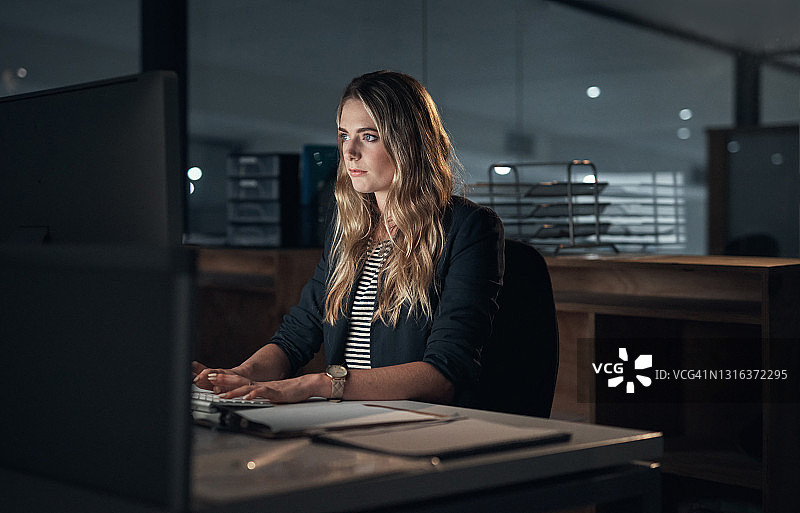 这是一个年轻的女商人深夜在现代办公室里使用电脑的照片图片素材