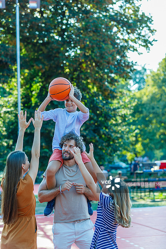 一个快乐的家庭正在操场上玩篮球。图片素材