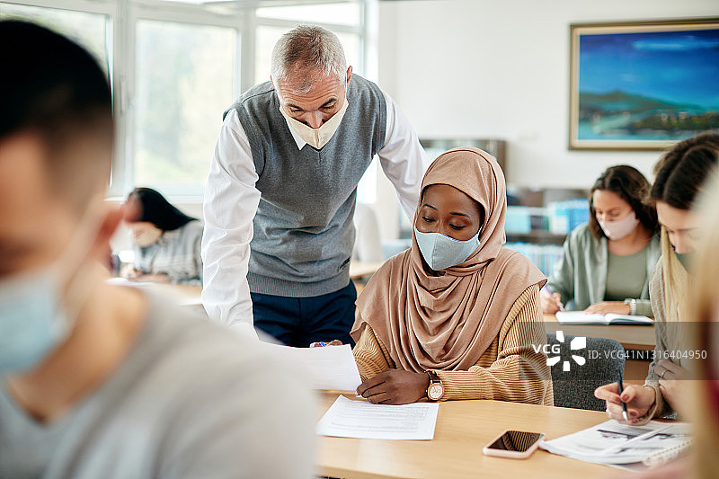 成熟的教师在课堂上戴着口罩协助穆斯林女学生讲课。图片素材
