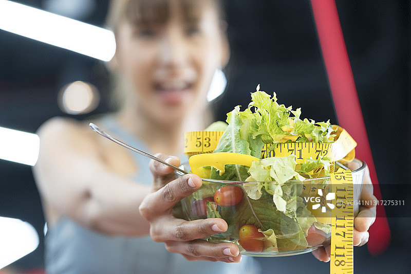 健康的食物，年轻女子拿着碗里的沙拉，喜欢在健身房吃沙拉。图片素材