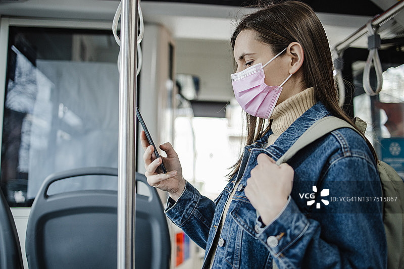 戴着保护面罩的妇女在公共交通工具上使用手机图片素材