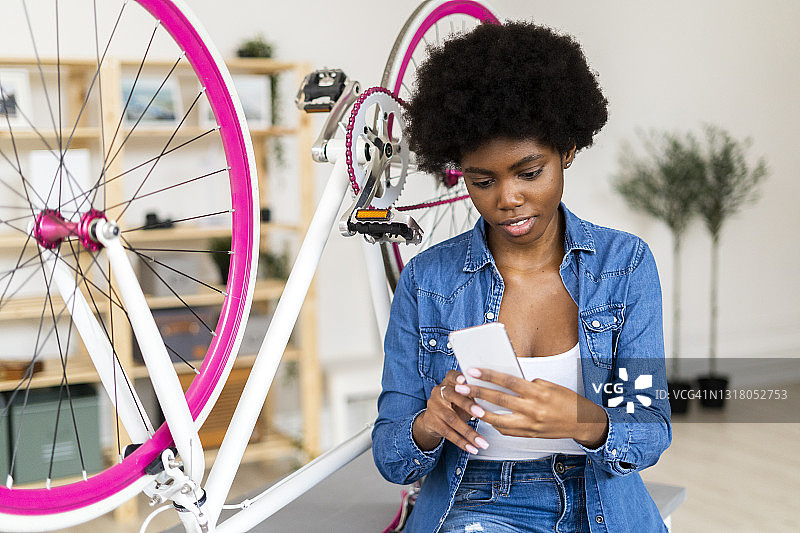 年轻女子在家里的桌子上，坐在自行车旁使用手机图片素材