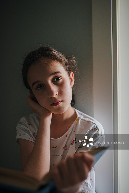 一个蓝眼睛的白人女孩在黄昏时坐在她家走廊的地板上看书的特写。图片素材