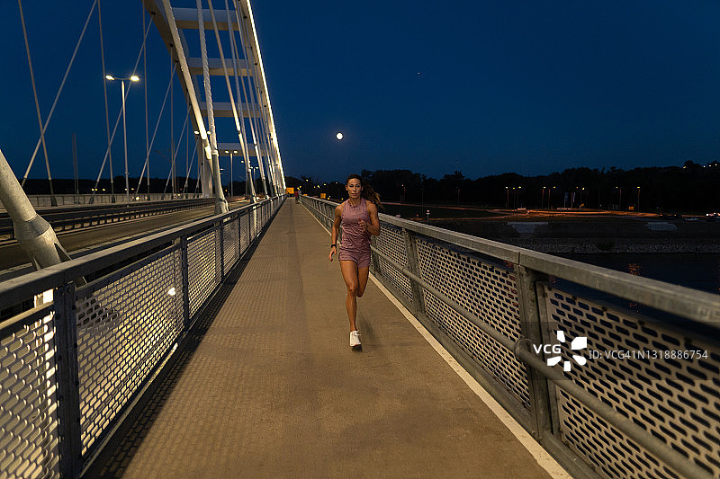 年轻的女运动员晚上在桥上奔跑图片素材