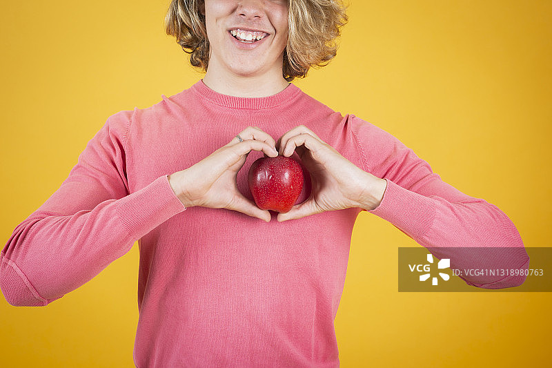 半边微笑的男人拿着一个红苹果，双手放在一颗心之间图片素材