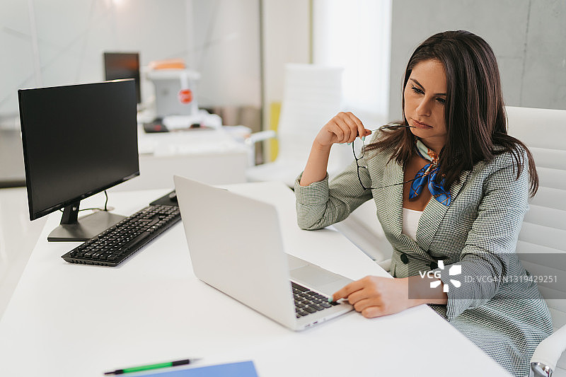 年轻的商业女性坐在现代的办公室里，用笔记本电脑工作图片素材