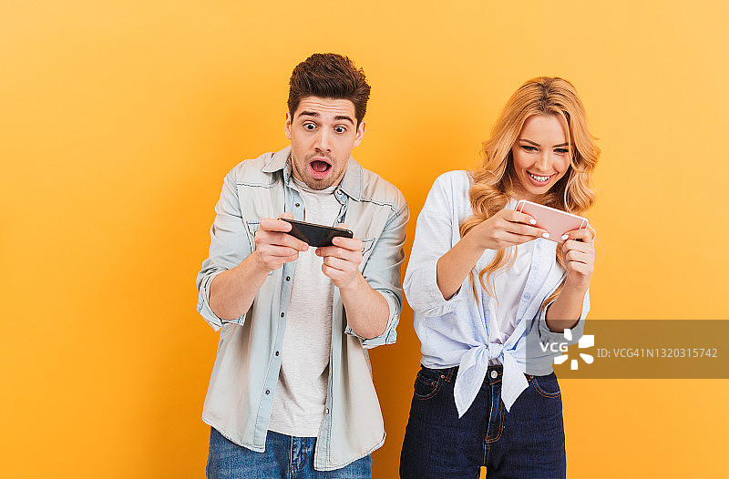 这是一对有趣的年轻男女一起玩手机视频游戏的画面，黄色的背景使他们与世隔绝图片素材