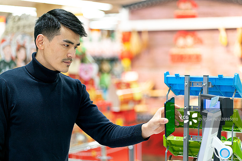 亚洲男性顾客在杂货店用手机扫描二维码进行非接触式支付图片素材