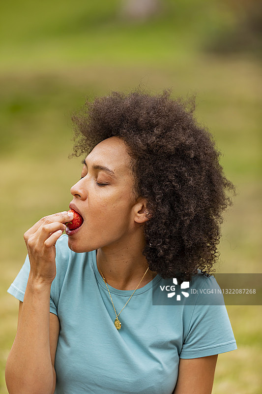 一个卷头发的女人在户外散步并吃草莓。图片素材