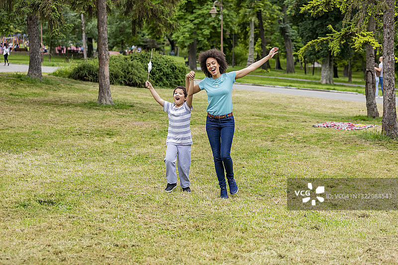 快乐的非裔美国妇女和她可爱的儿子在公园里散步。图片素材