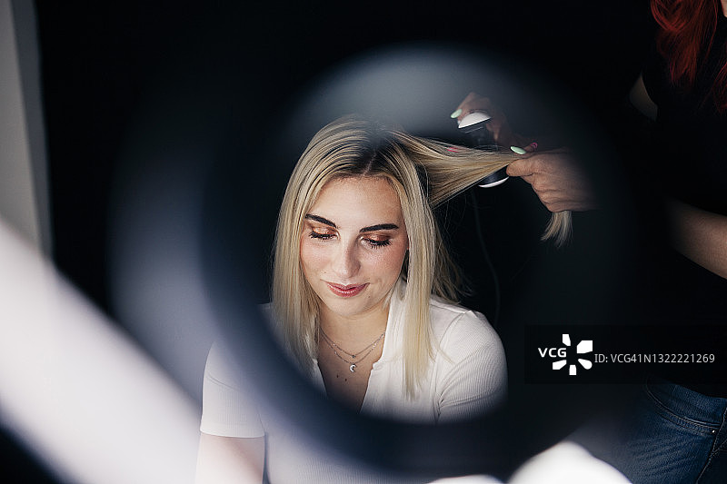 女发型师使用直发器通过环光看到美丽的模特的头发图片素材
