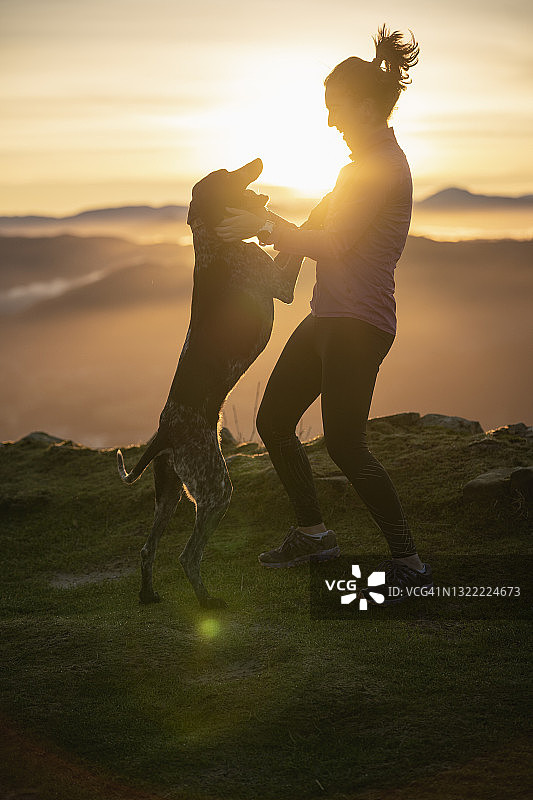 日出时分，一个女人在山上和狗狗玩耍图片素材