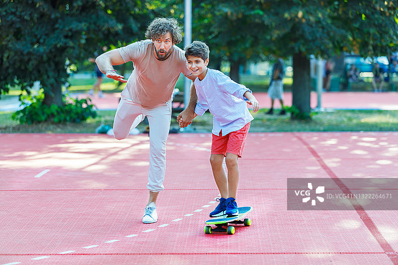 一位年轻的父亲和他的儿子在公园里玩滑板。图片素材