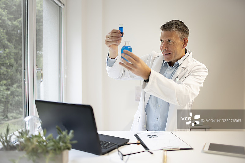 男性化学家、科学家在高台上工作，检查小瓶子里的蓝色液体图片素材