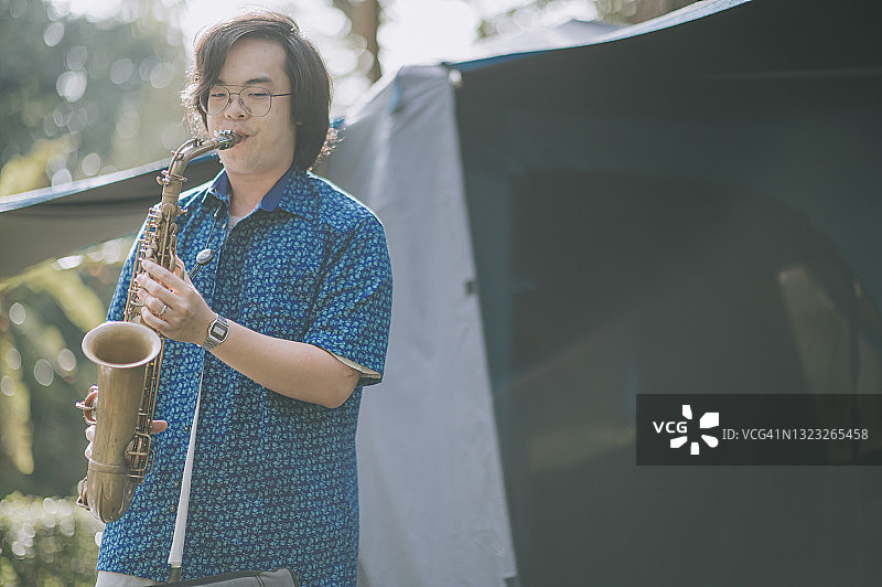 亚洲华人萨克斯风吹奏者在露营帐篷前演奏图片素材