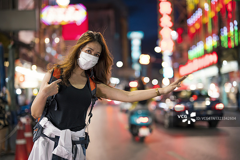 独自旅行的亚洲女人戴着口罩和背包在曼谷唐人街市场街头等待出租车的夜生活。图片素材