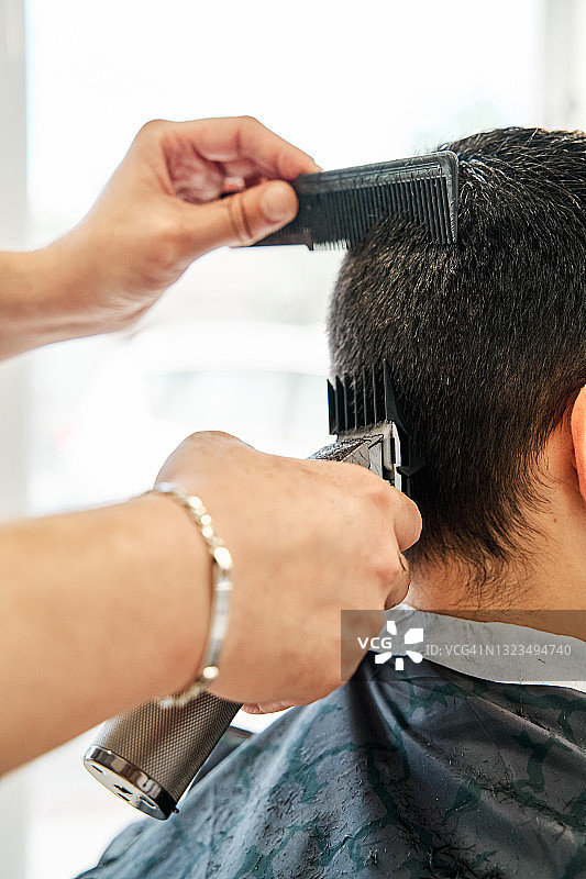 一个年轻男子在理发店的机器理发的细节视图。图片素材
