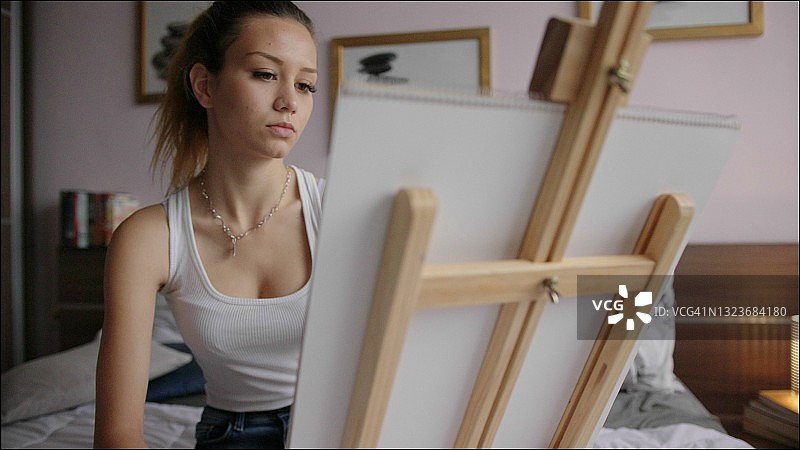 年轻女子在卧室里画画。艺术家在家工作。2019冠状病毒肺炎大流行封锁期间不要外出。图片素材