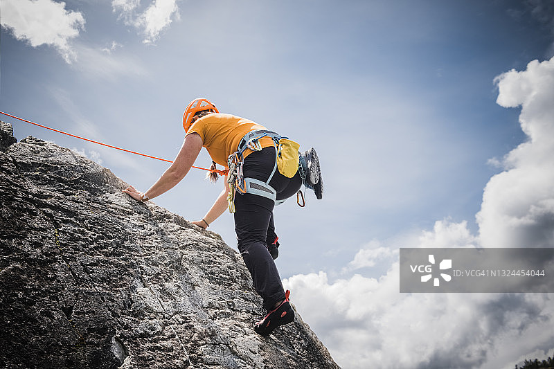 仰望一位女攀岩者，她正攀爬着高高的岩壁，头顶是蓝天图片素材