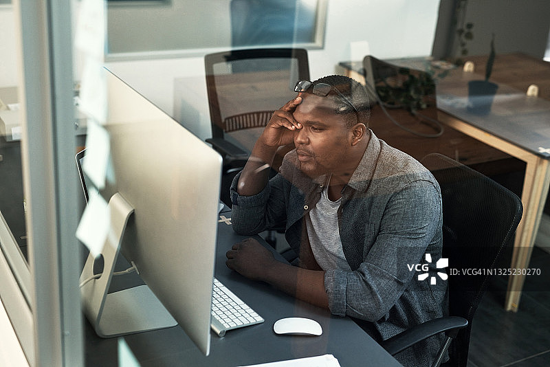 一个英俊的年轻商人独自坐在办公室里，在使用他的电脑时感到压力图片素材