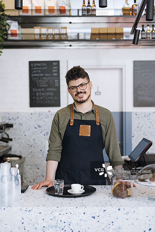 微笑的服务员站在一个咖啡店的柜台后面的肖像图片素材
