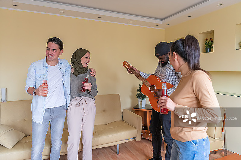 一群年轻的多元文化朋友在家里享受吉他之声和舞蹈。图片素材