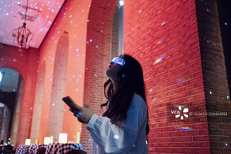 一名女子戴着增强现实眼镜，用智能手机站在夜间的街道上图片素材
