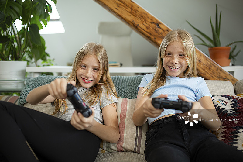 一对快乐的白种双胞胎姐妹在家里玩电子游戏图片素材