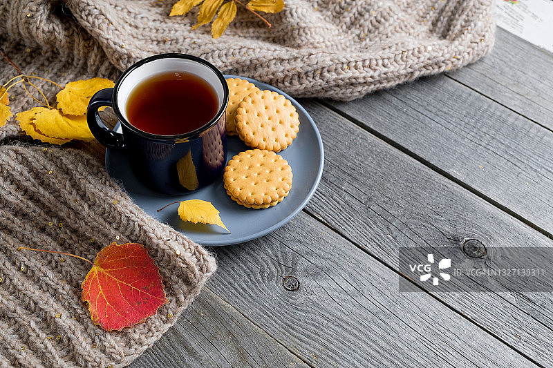 热咖啡或茶在杯中，饼干或甜点，明亮的秋天黄叶，温暖舒适的针织羊毛围巾，在木背景或桌子。季节性的娱乐、放松和心灵的平静的概念。文本空间的拷贝。图片素材