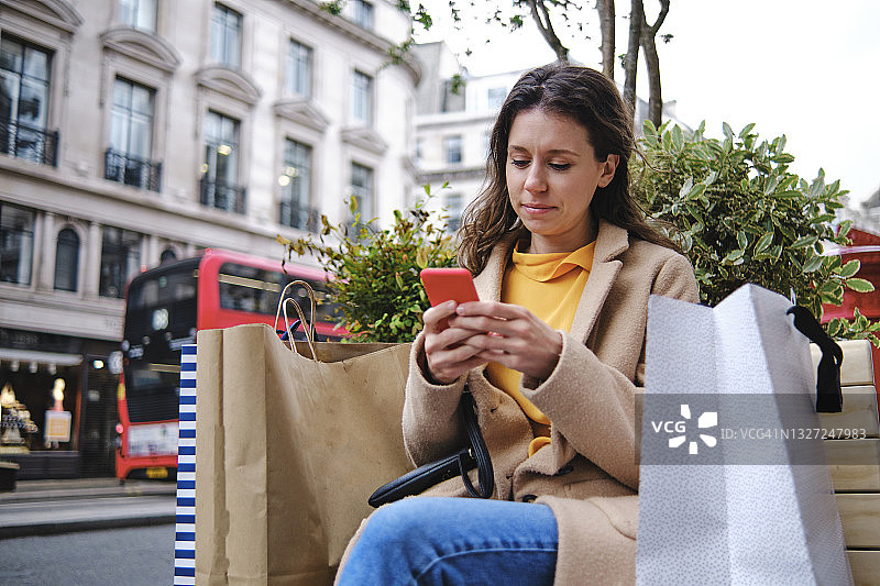 年轻女子用购物袋在城市里使用智能手机图片素材