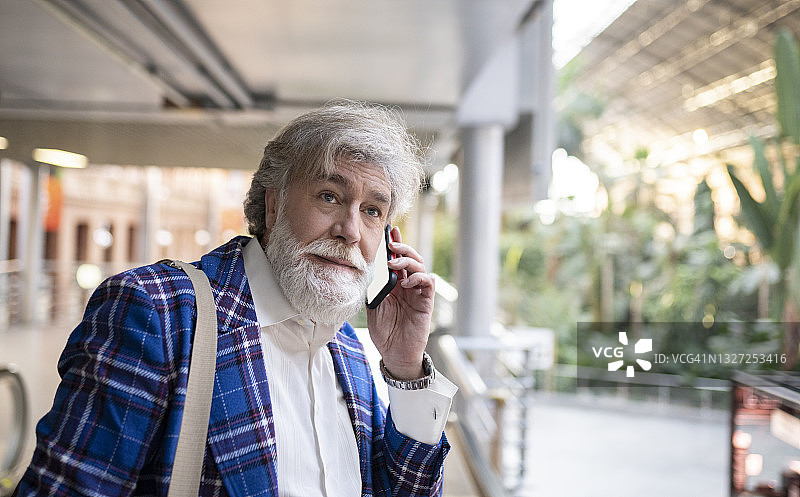 一个成熟的白胡子男人在车站打电话的时候看向别处图片素材